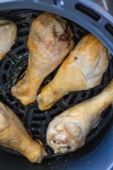 Four perfectly cooked air fryer chicken drumsticks nestled inside a basket, showcasing their crispy, golden-brown exterior.