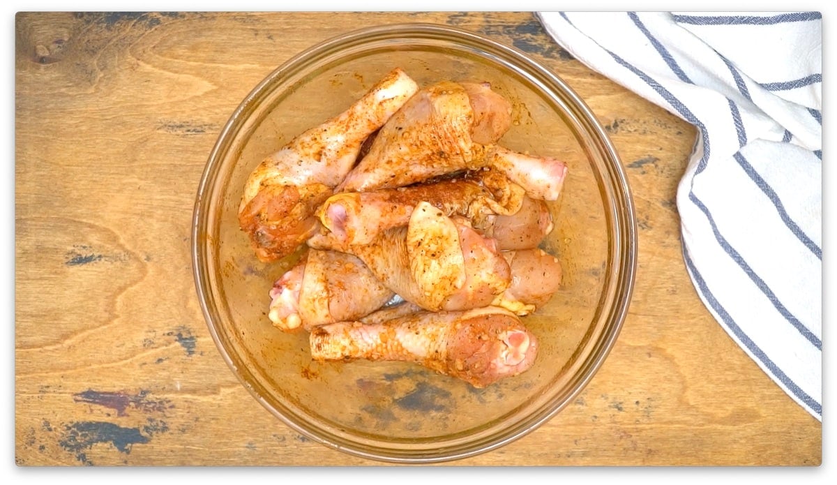 picture of seasoned raw chicken drumsticks in a glass bowl