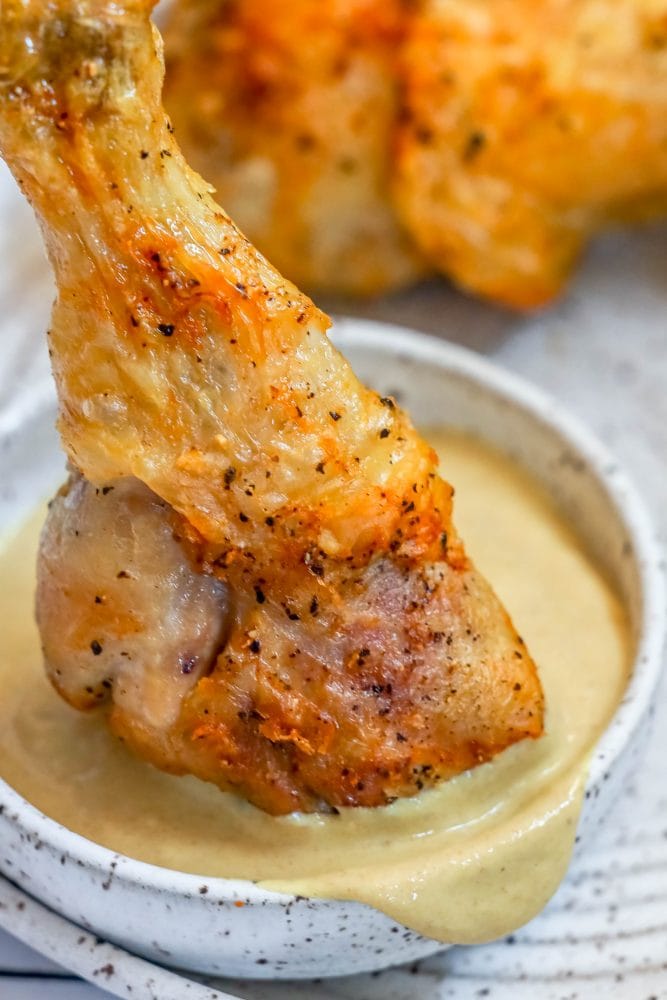 Air fried chicken legs in a white bowl with a sauce.