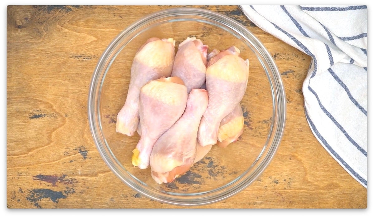 Chicken legs cooked in an air fryer, displayed in a glass bowl on a wooden table.