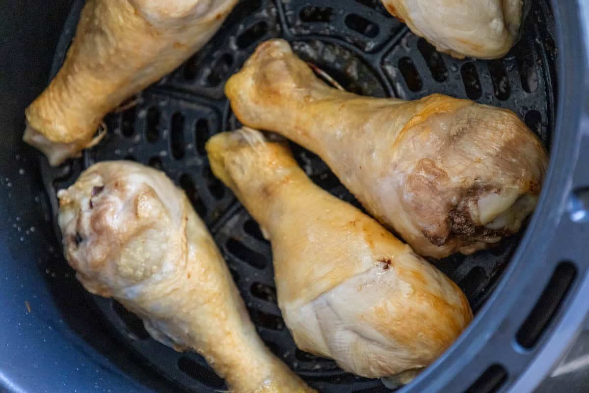 Four easy chicken drumsticks rest in an air fryer basket, perfectly poised for a crispy golden finish.