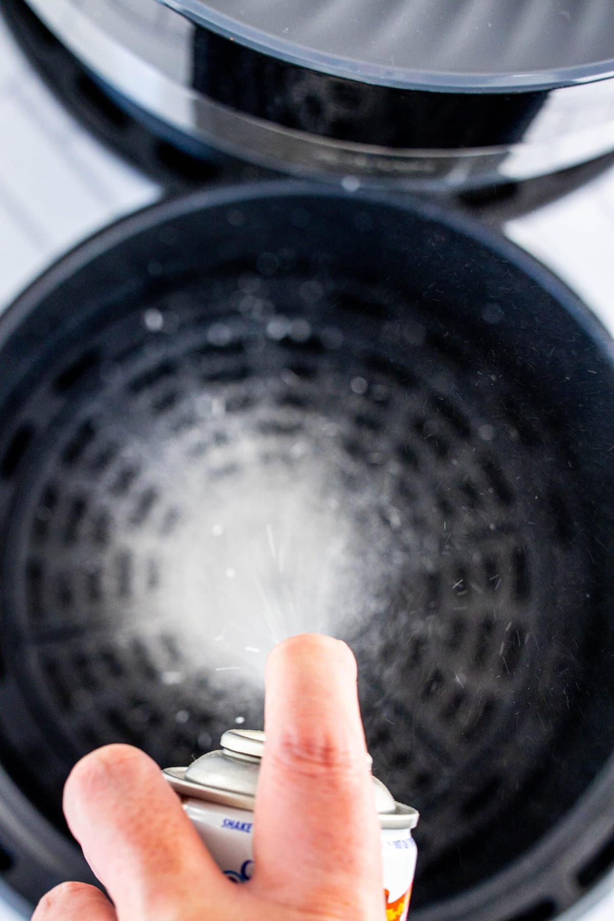 picture of hand spraying nonstick spray into air fryer basket
