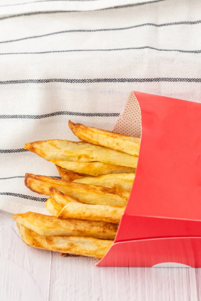 Crispy air fried French fries in a red box on a wooden table.