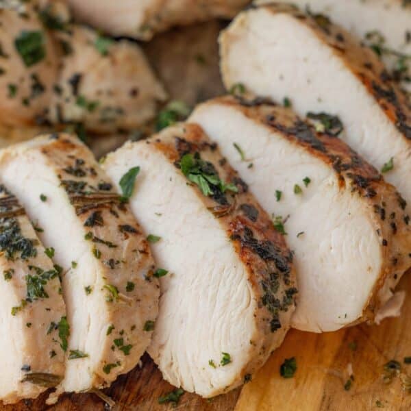 Sliced cooked chicken breast garnished with chopped herbs on a wooden cutting boardโa presentation perfect for showcasing an Easy Turkey Recipe or Baked Turkey Tenderloin as well.