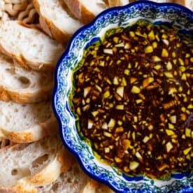 A bowl of olive oil and balsamic vinaigrette dip with chopped garlic is surrounded by slices of crusty bread.