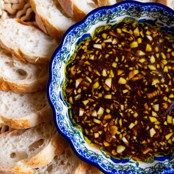 A bowl of olive oil and balsamic vinaigrette dip with chopped garlic is surrounded by slices of crusty bread.