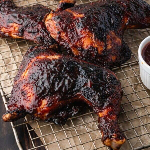 Grilled barbecue chicken quarters on a wire rack with a small bowl of barbecue sauce on the side.