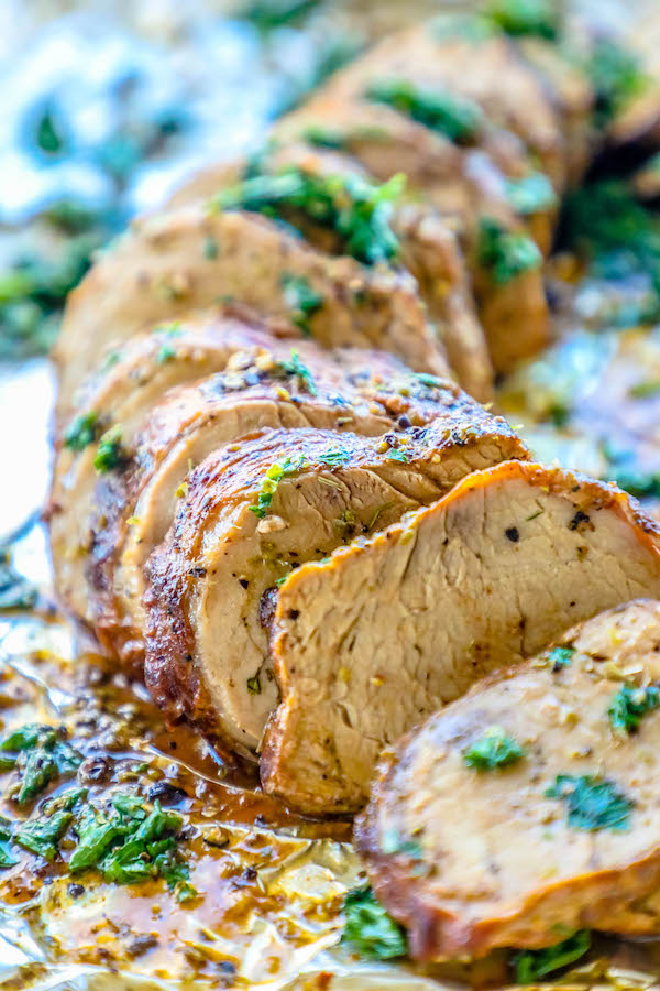 Picture of pork tenderloin sliced and garnished with parsley on tinfoil.
