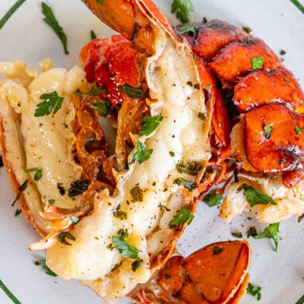 Close-up of a butter poached lobster tail in garlic cream sauce, garnished with herbs and served on a white plate.