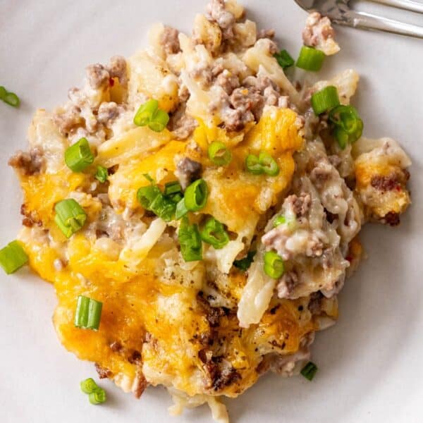 A serving of cheesy ground beef hashbrown casserole with chopped green onions on a white plate.