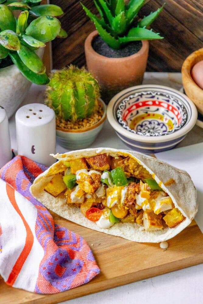 A chicken shawarma pita on a wooden cutting board.
