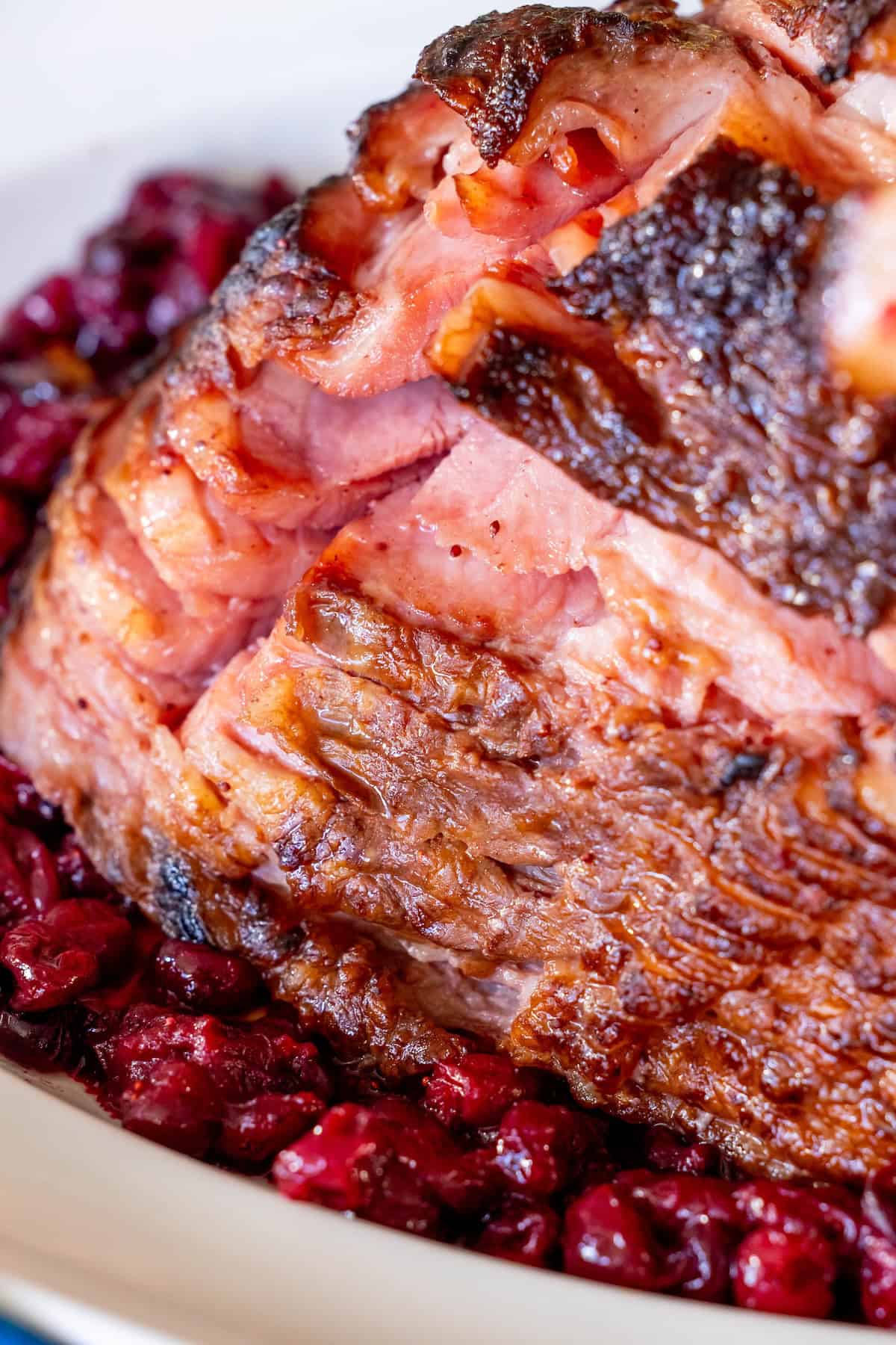 Close-up of a glazed spiral ham served on a bed of cooked cranberries in a white dish, with hints of cranberry brandy enhancing its rich flavor.