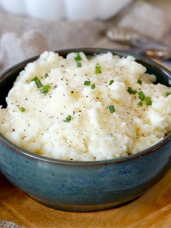 A bowl of creamy mashed potatoes on a cutting board.
