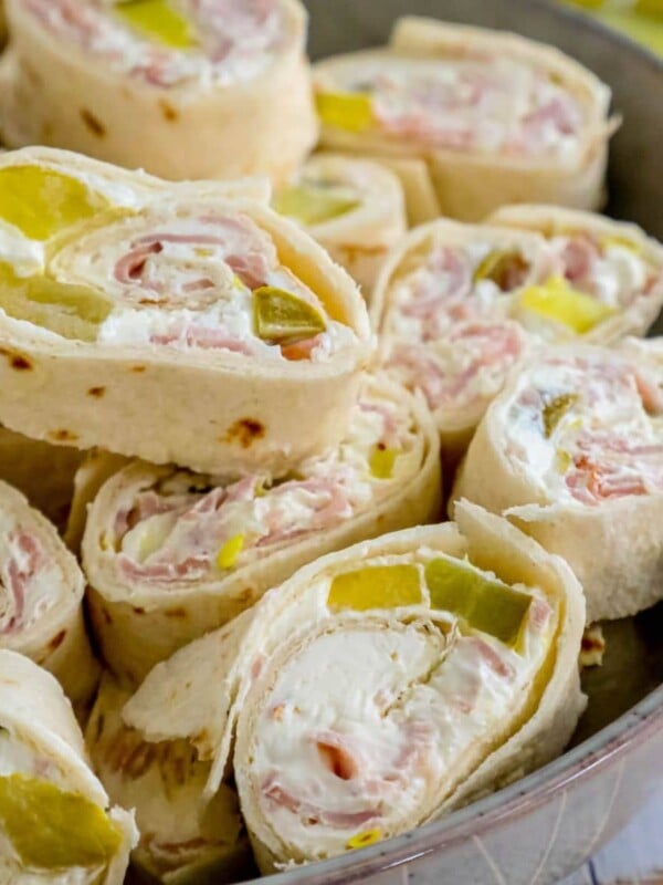 sliced pinwheel sandwiches in tortillas with cream cheese, ham, and pickles stacked in a metal bowl