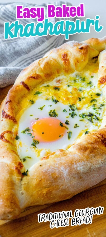 picture of baked khachapuri cheese bread on a wood cutting board with egg yolk and herbs on top