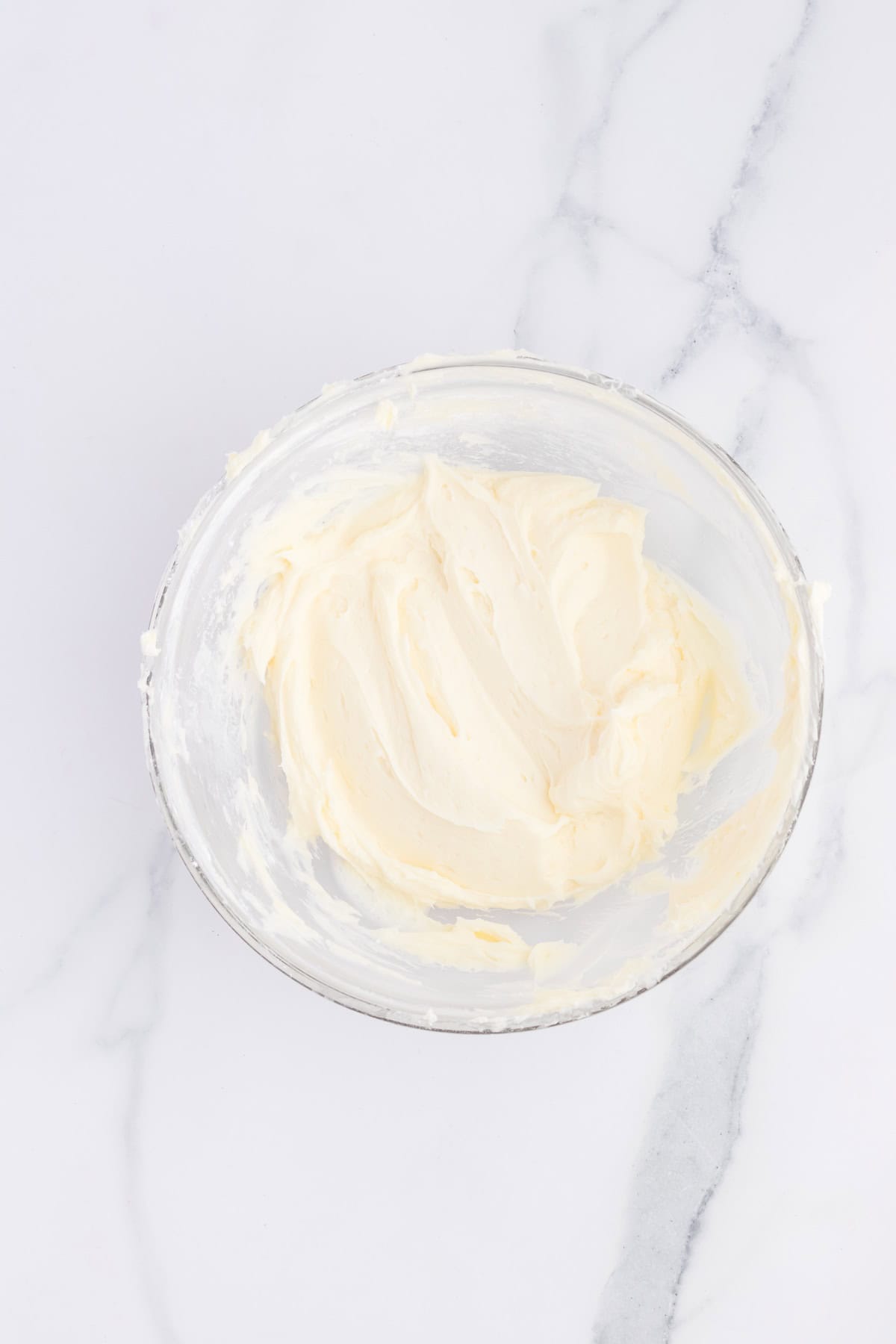 A bowl of creamy, smooth frosting sits on a marble countertop, perfectly primed for decorating your favorite cupcakes.