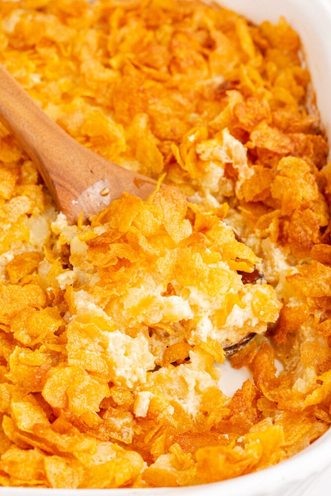 A crunchy funeral potato casserole dish with a wooden spoon in it.