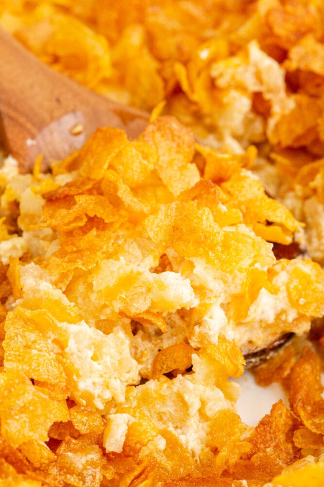 A wooden spoon is being used to scoop up a cheesy hashbrown casserole.