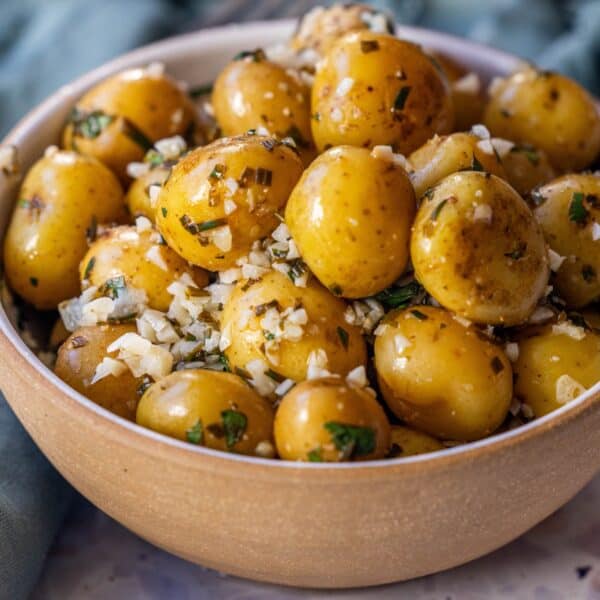 A bowl filled with seasoned chive potatoes, garnished with chopped herbs and minced garlic, makes a delicious garlic potatoes dish.