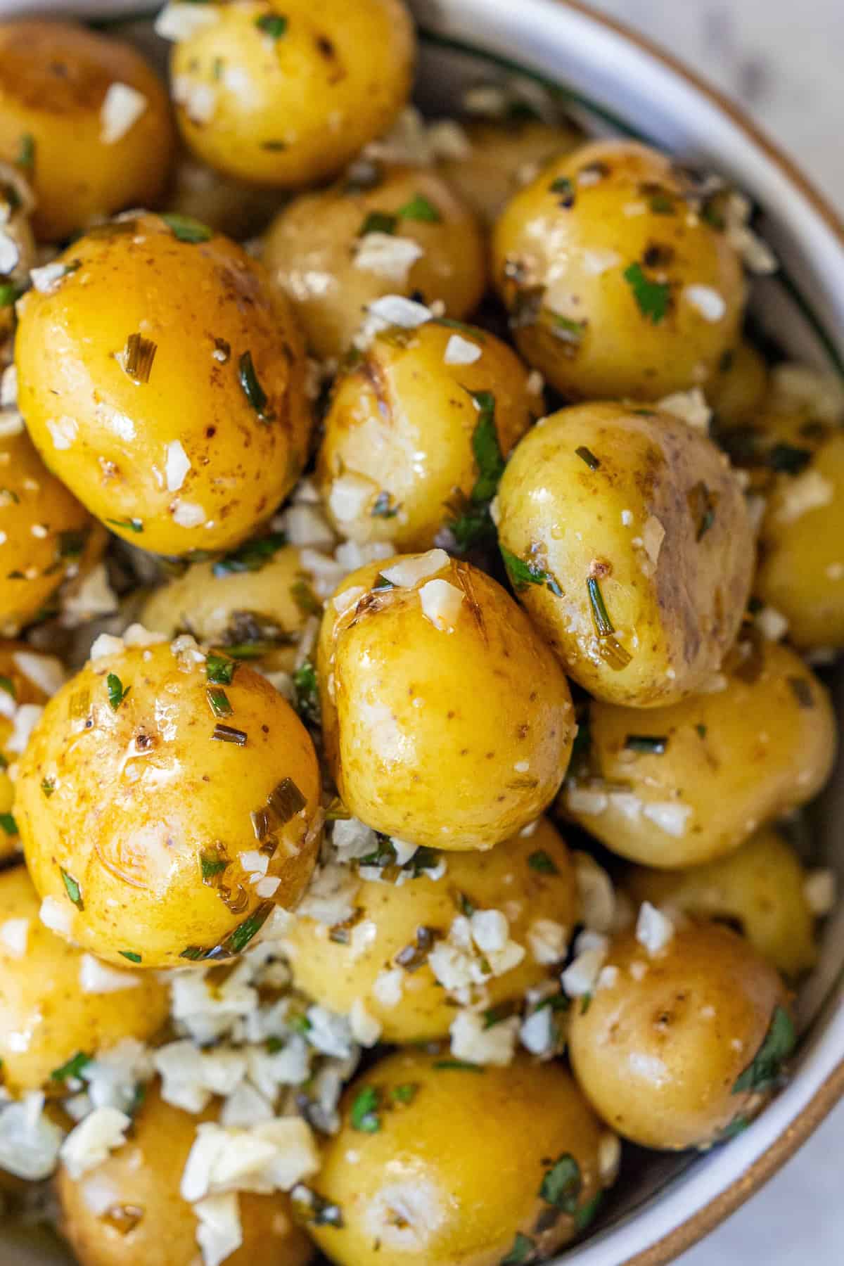 A bowl of cooked garlic and chive potatoes, garnished with chopped herbs and minced garlic.