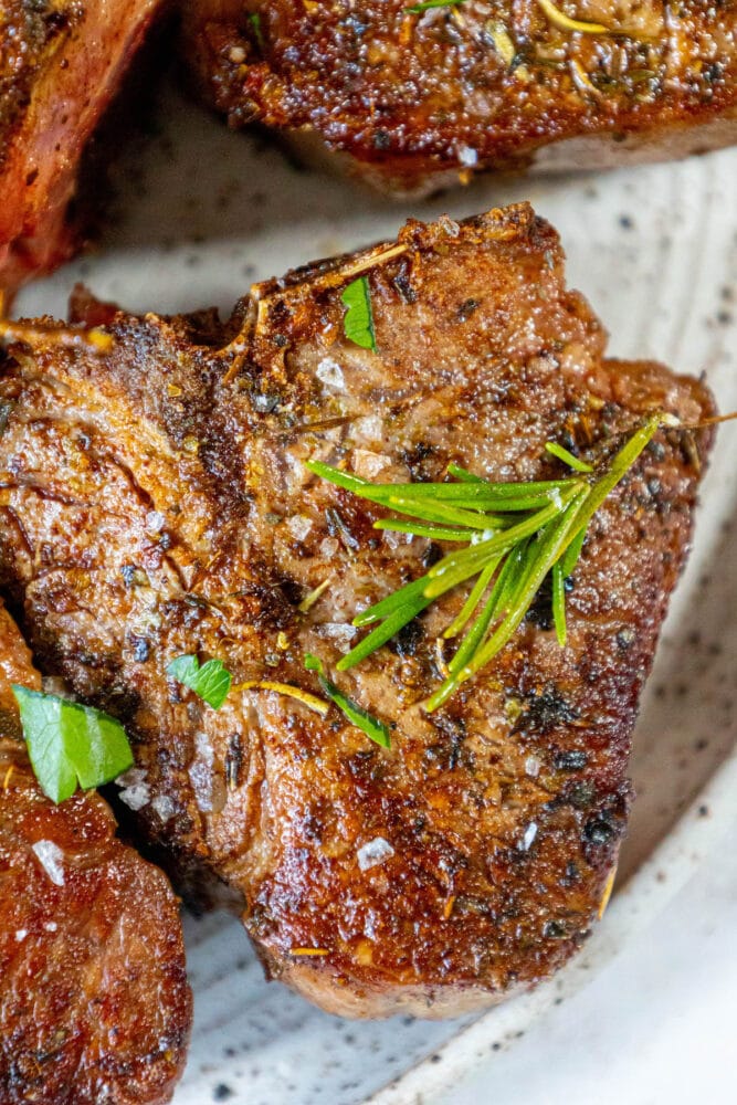 Grilled lamb chops on a plate with rosemary sprigs, garlic butter seared.