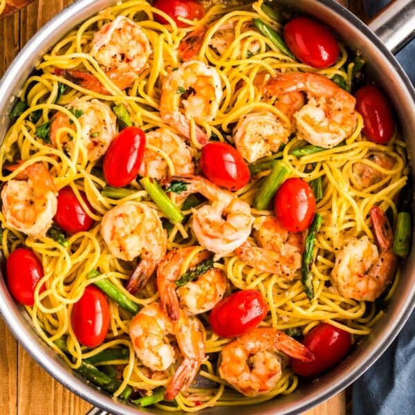 A pan of shrimp spaghetti with cherry tomatoes and asparagus, seasoned with fresh herbs and a hint of garlic.