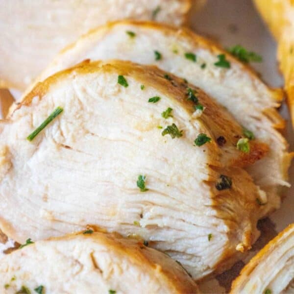 Close-up of sliced, cooked chicken breast garnished with chopped herbs. The chicken, marinated in a succulent greek grilled chicken marinade, is lightly seared and appears tender and moist.
