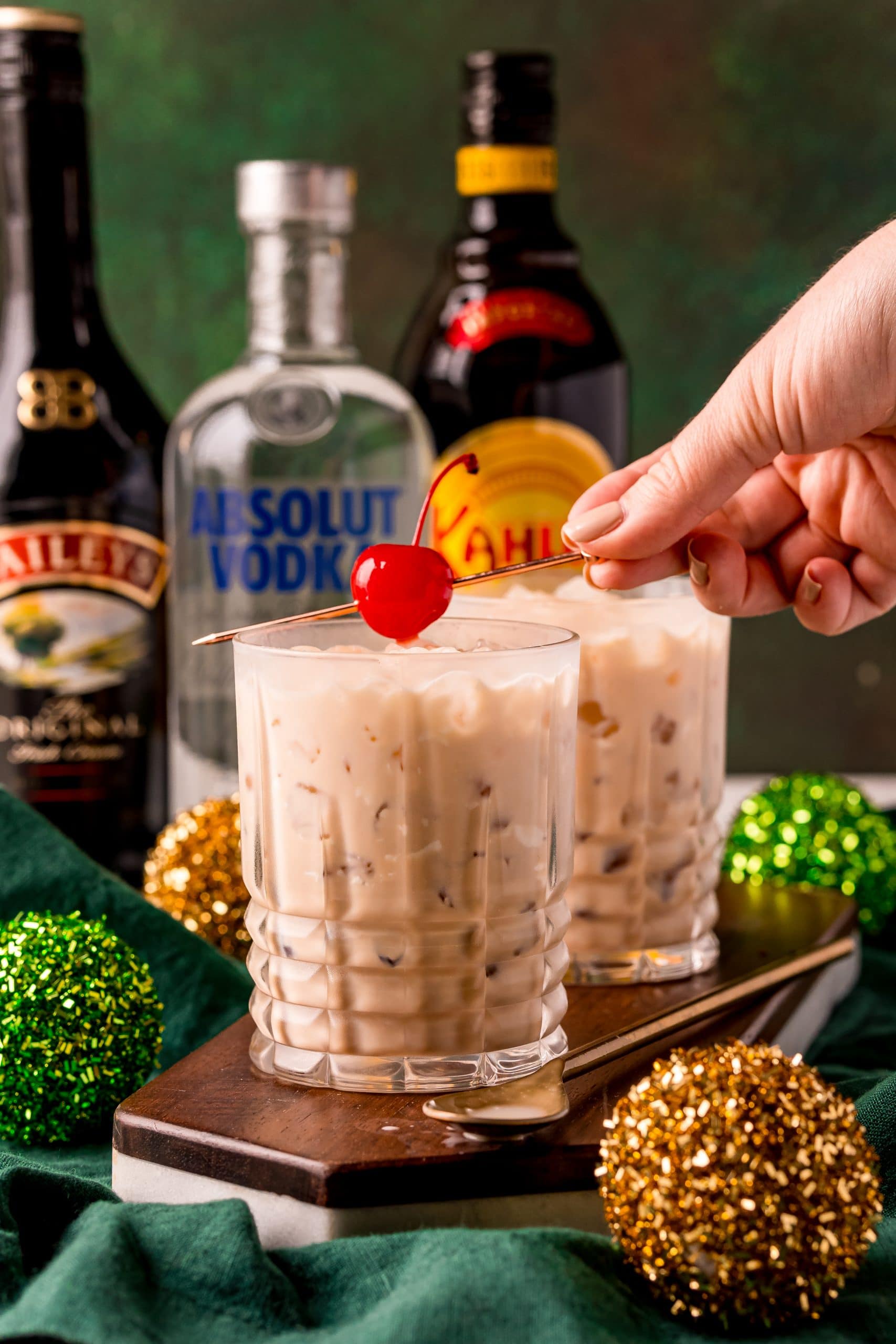 A person is holding an Irish Cream cocktail with a cherry on top.