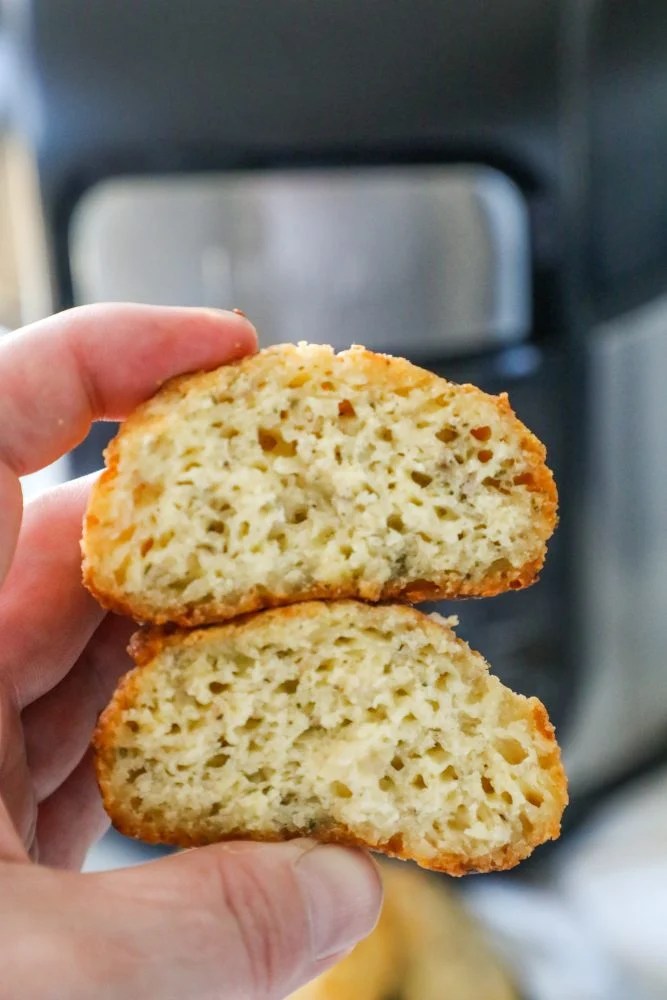 A person holding a piece of bread in front of an air fryer while making keto rolls.