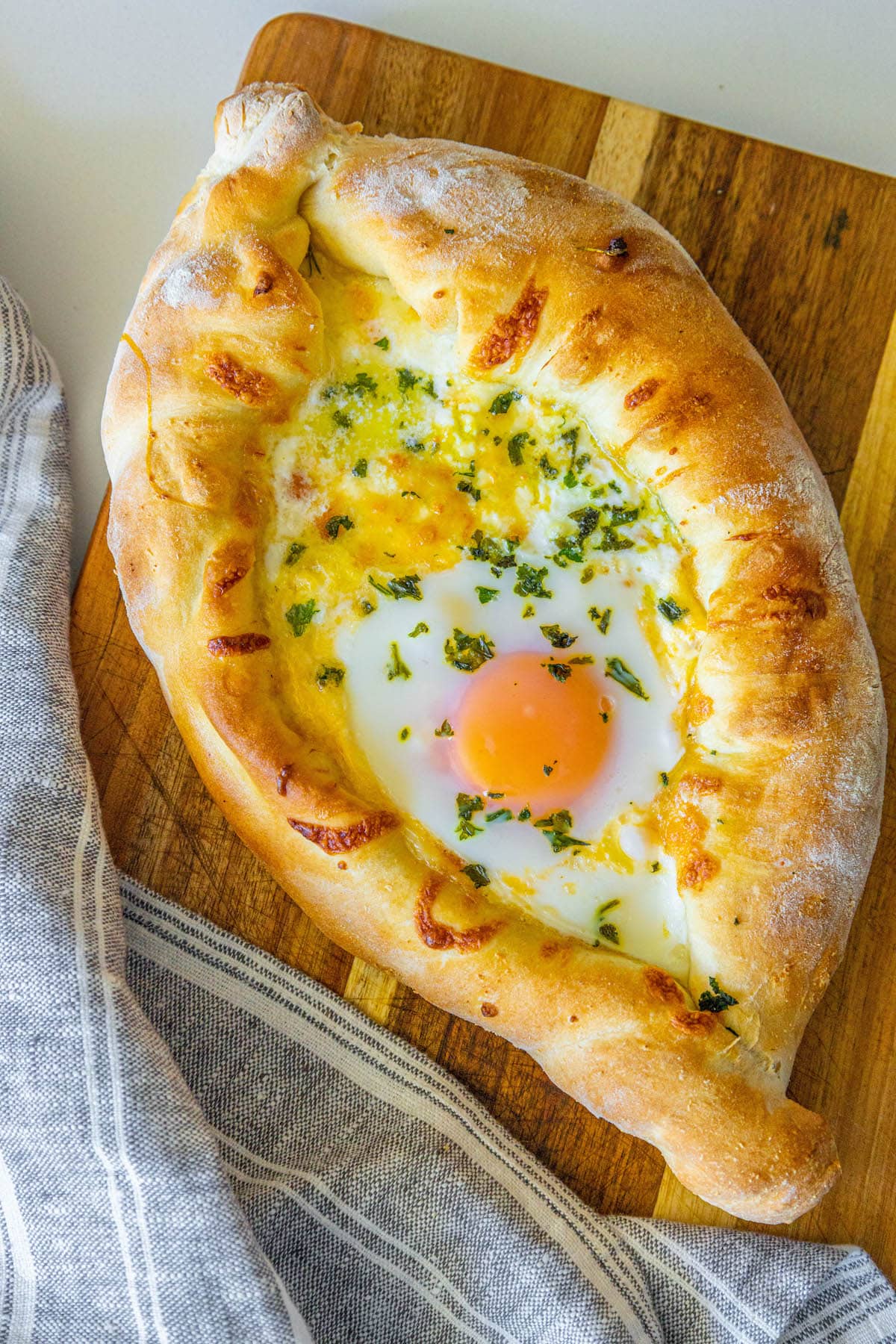 A Khachapuri, a traditional Georgian cheese bread recipe, with an egg atop it on a cutting board.