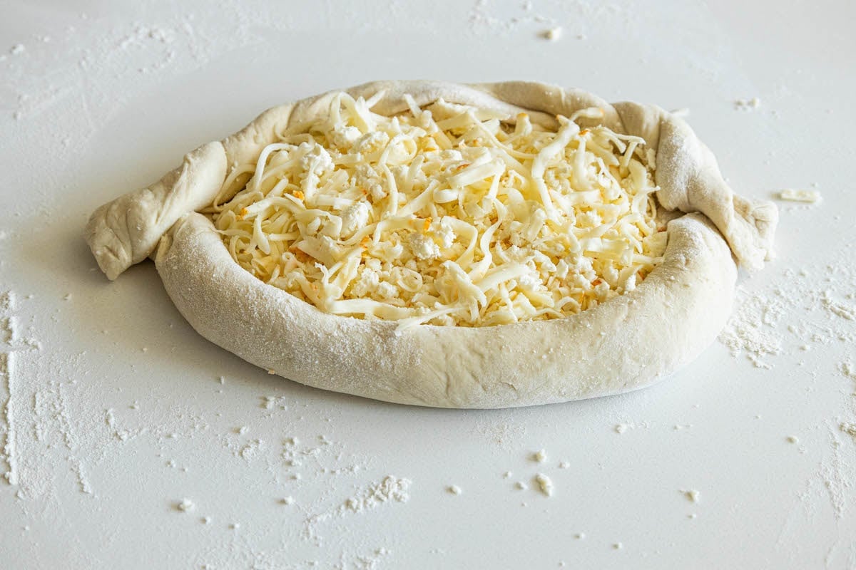 picture of raw dough with cheese on top of shaped khachapuri on table