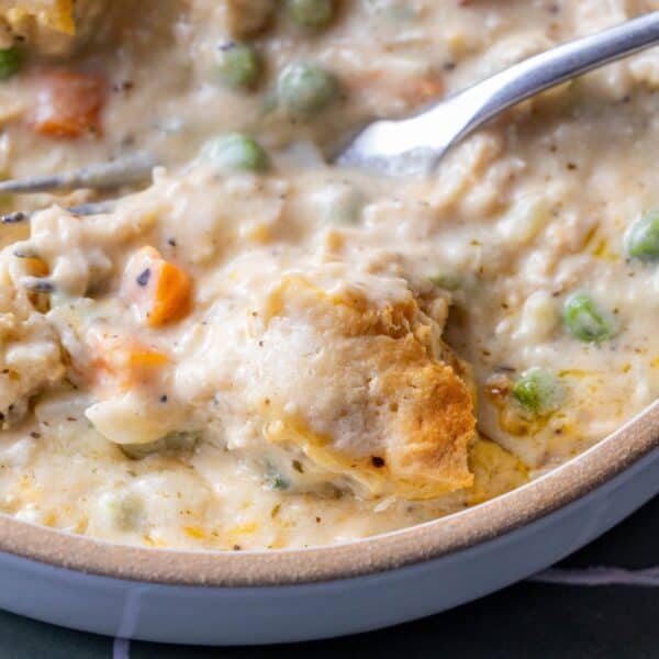 Close-up of a creamy biscuit casserole filled with chicken, vegetables, peas, and carrots, topped with biscuitsโperfect for using leftover turkeyโin a bowl with a spoon.