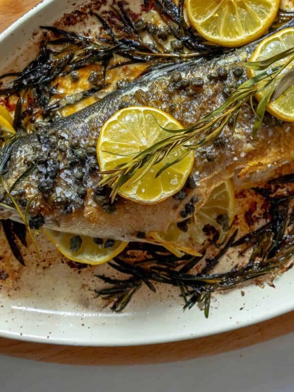 A Branzino on a plate with lemon slices and rosemary.