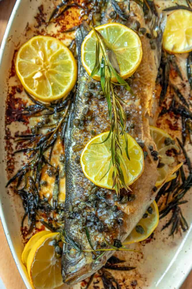 A lemon caper butter roasted branzino with rosemary on a plate.