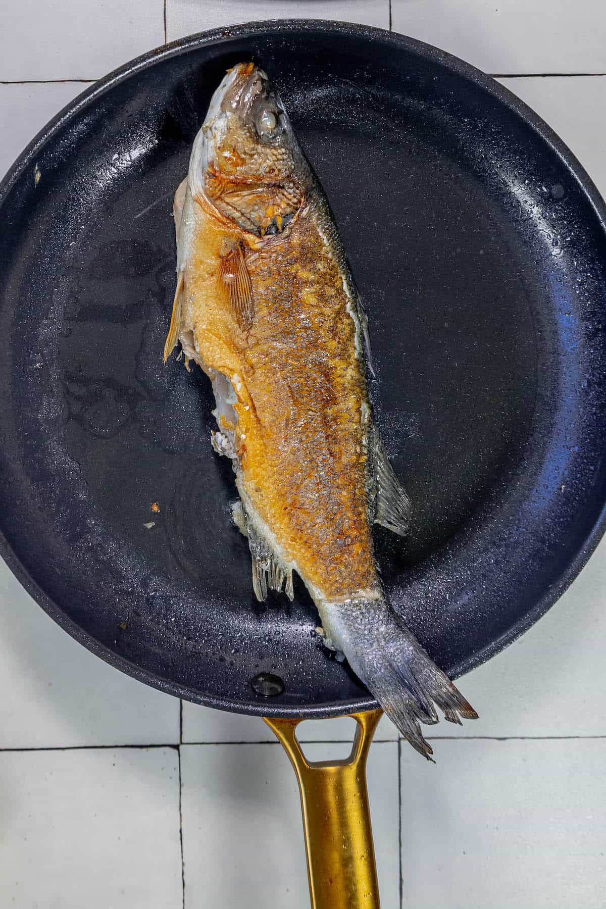 A Branzino fish is being cooked in a frying pan with lemon and butter.