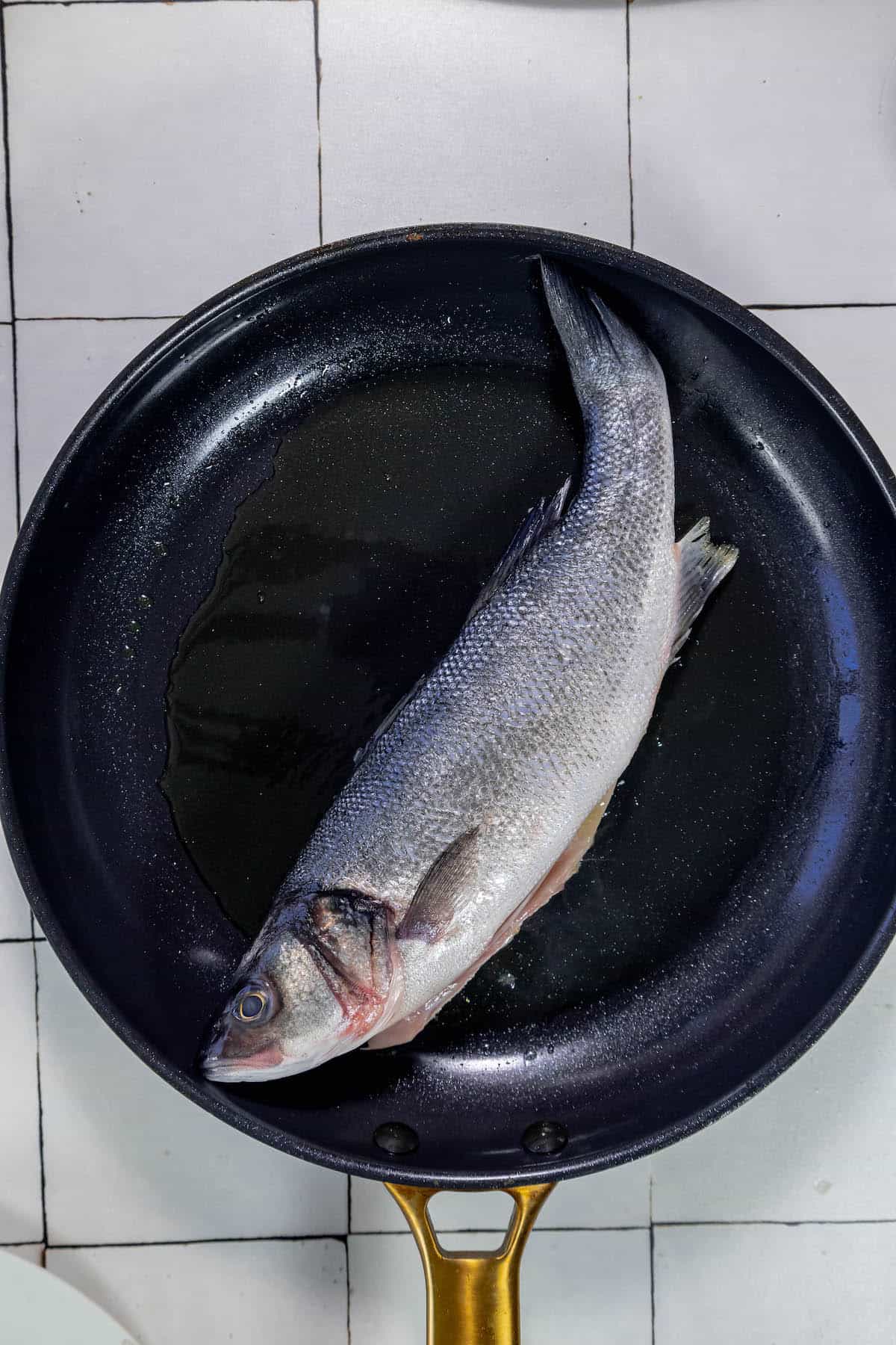 A Branzino fish is being cooked in a frying pan.
