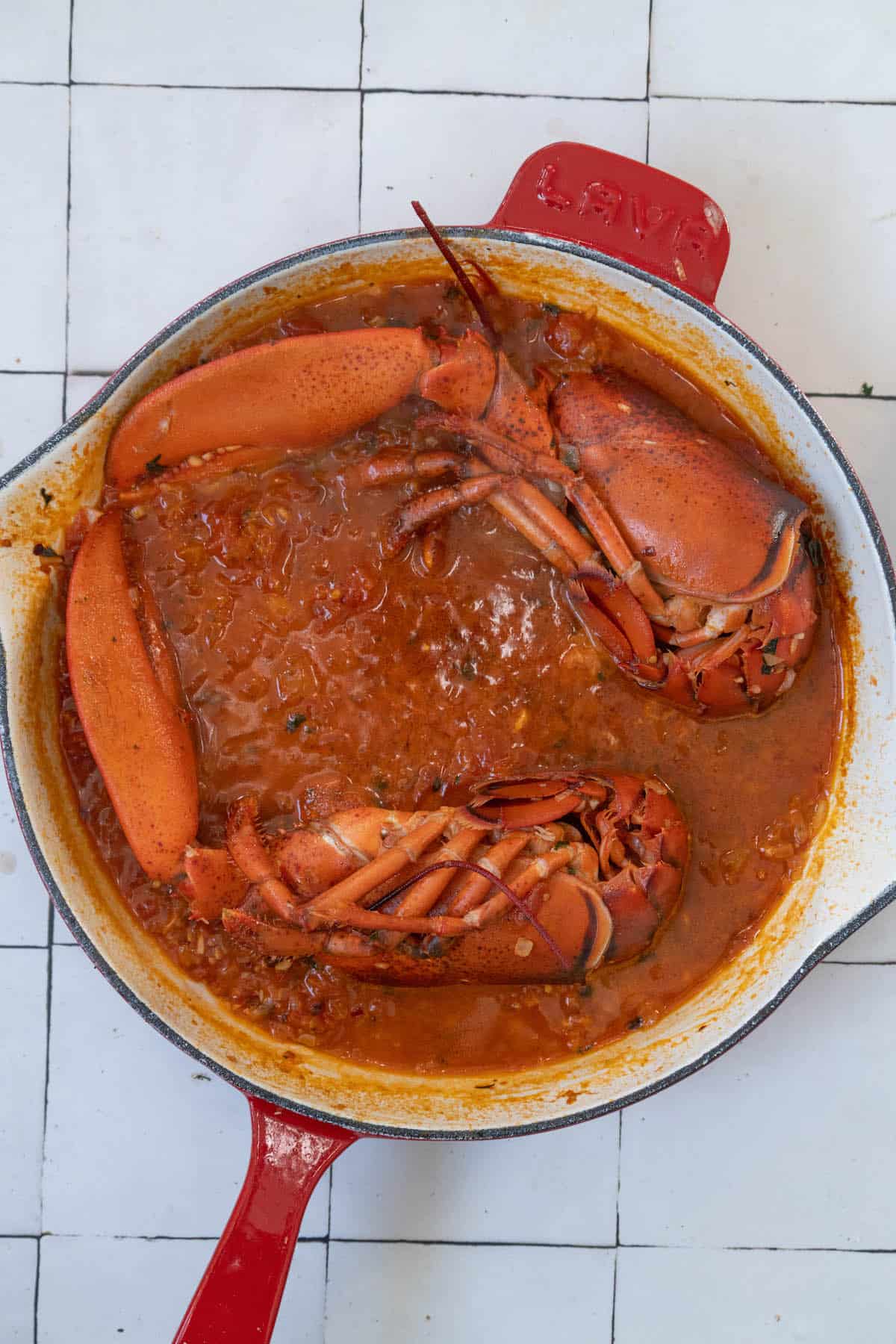 Two Venetian lobsters in a red skillet on a tiled floor.