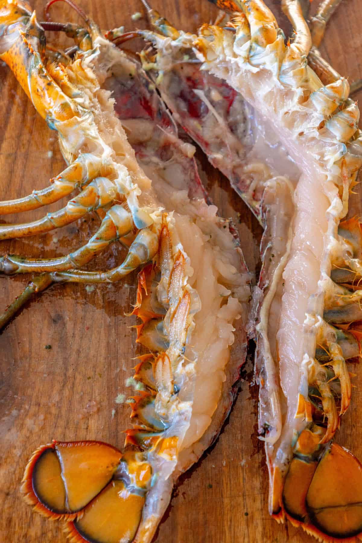 A Venetian lobster is sitting on a wooden cutting board, ready to be prepared as a delicious Busara Pasta.
