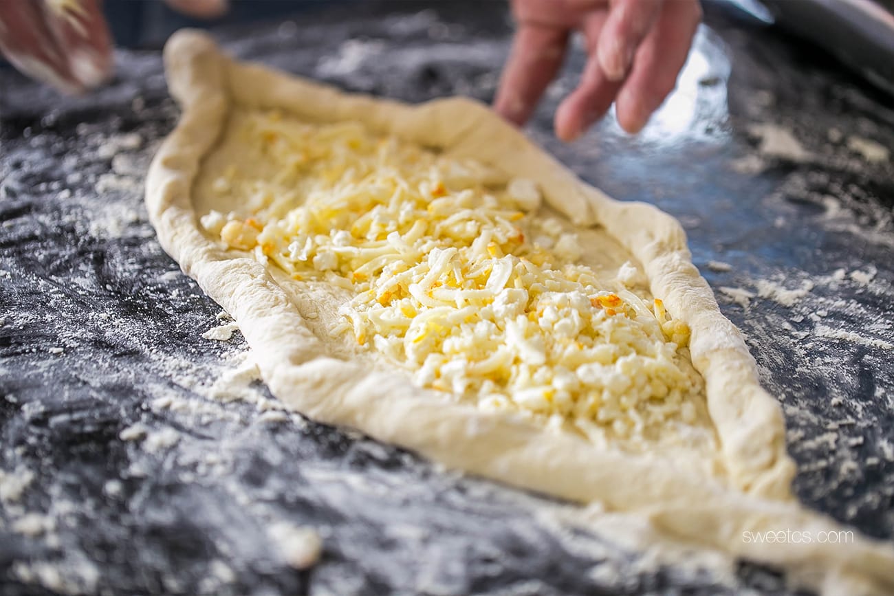A person is preparing Adjaruli khachapuri, a Georgian cheese bread, by putting cheese on pastry dough.