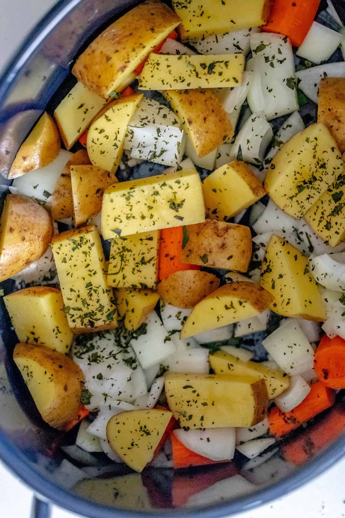 Chopped potatoes, carrots, onions, and herbs in a pot create the perfect base for a cozy pot roast recipe.