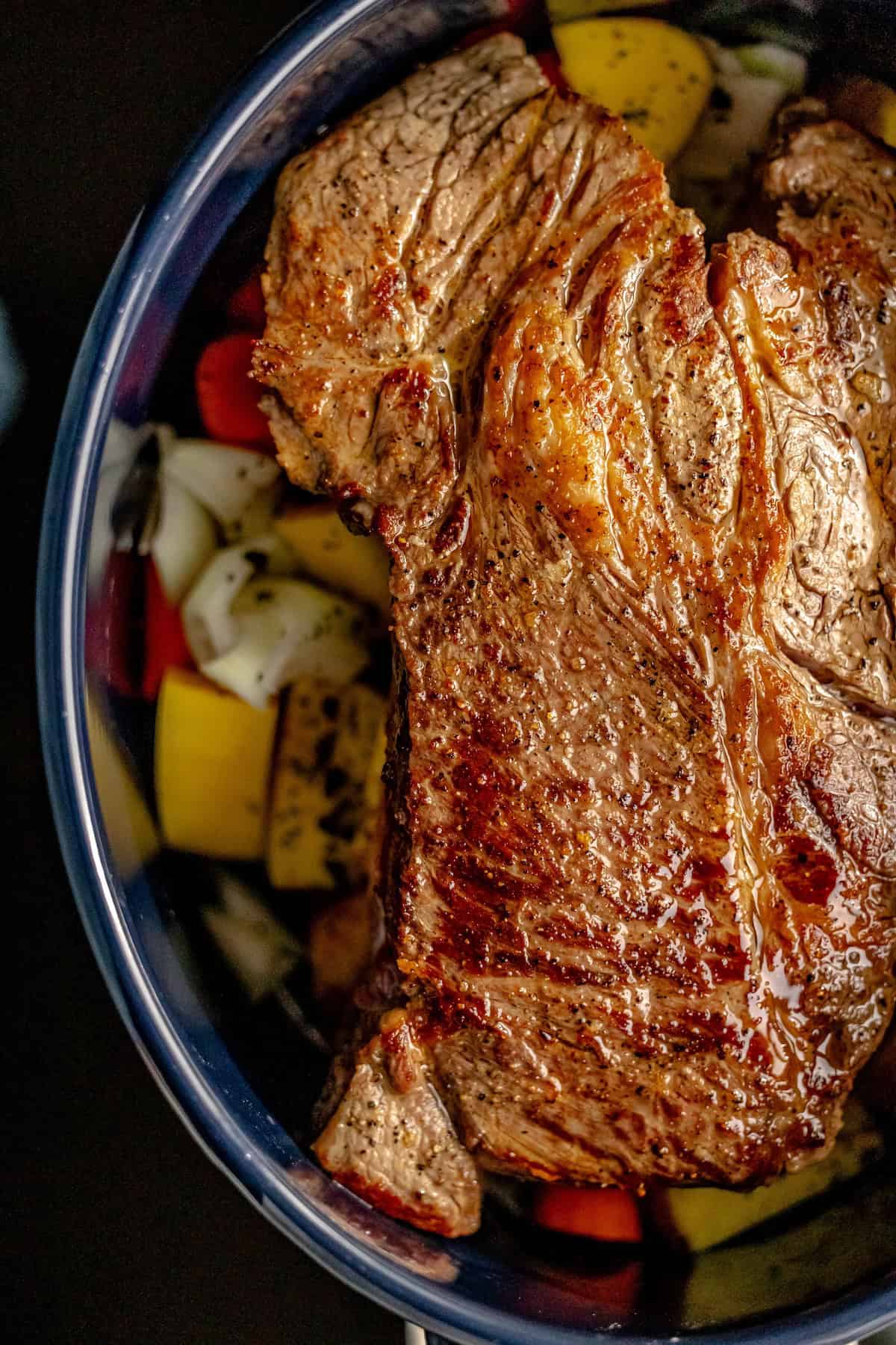 A succulent steak rests on a bed of caramelized onions, yellow bell peppers, and carrots, infused with the rich aroma of mushroom soup in a bowl.