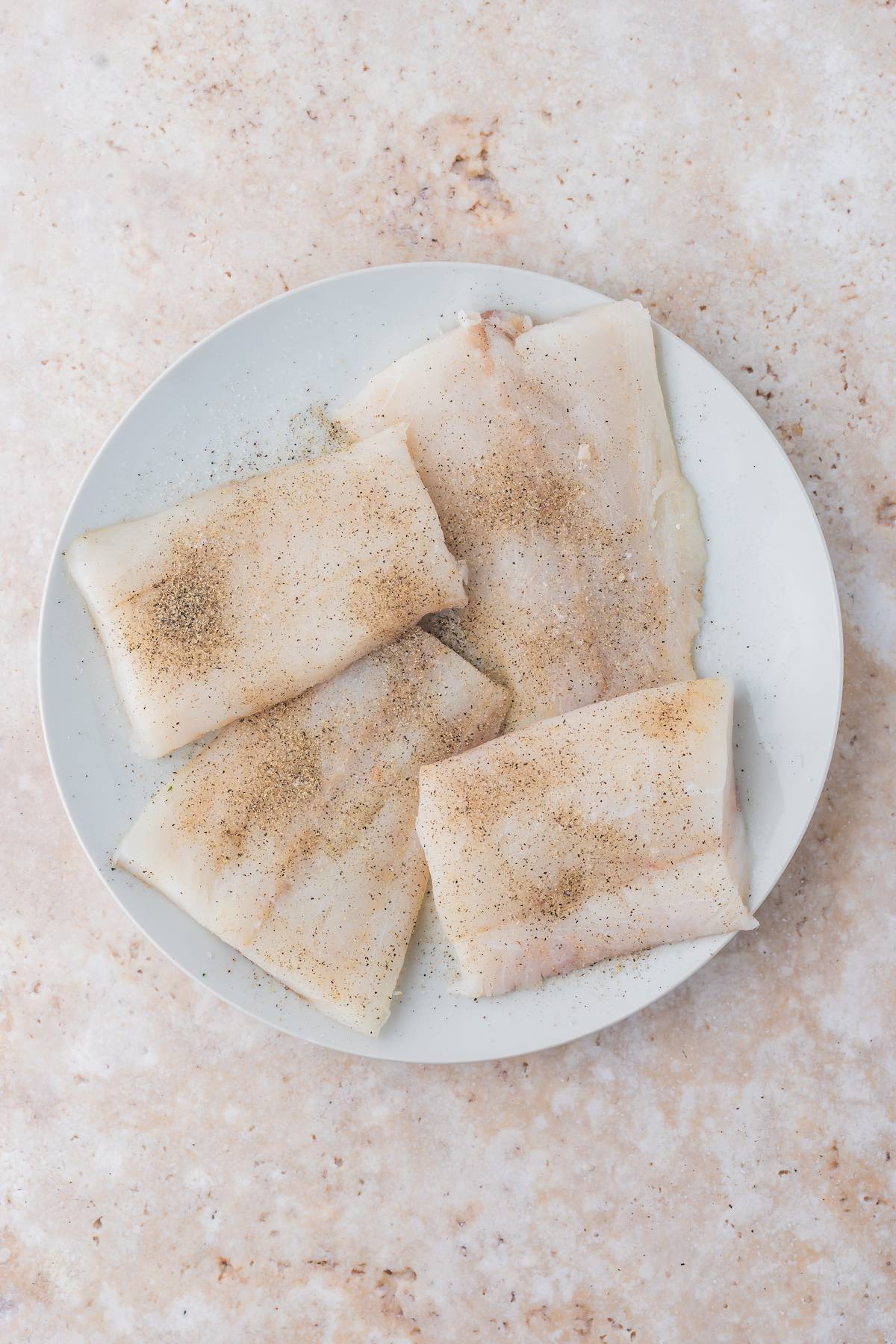 Pan-fried cod fillets on a plate with spices.
