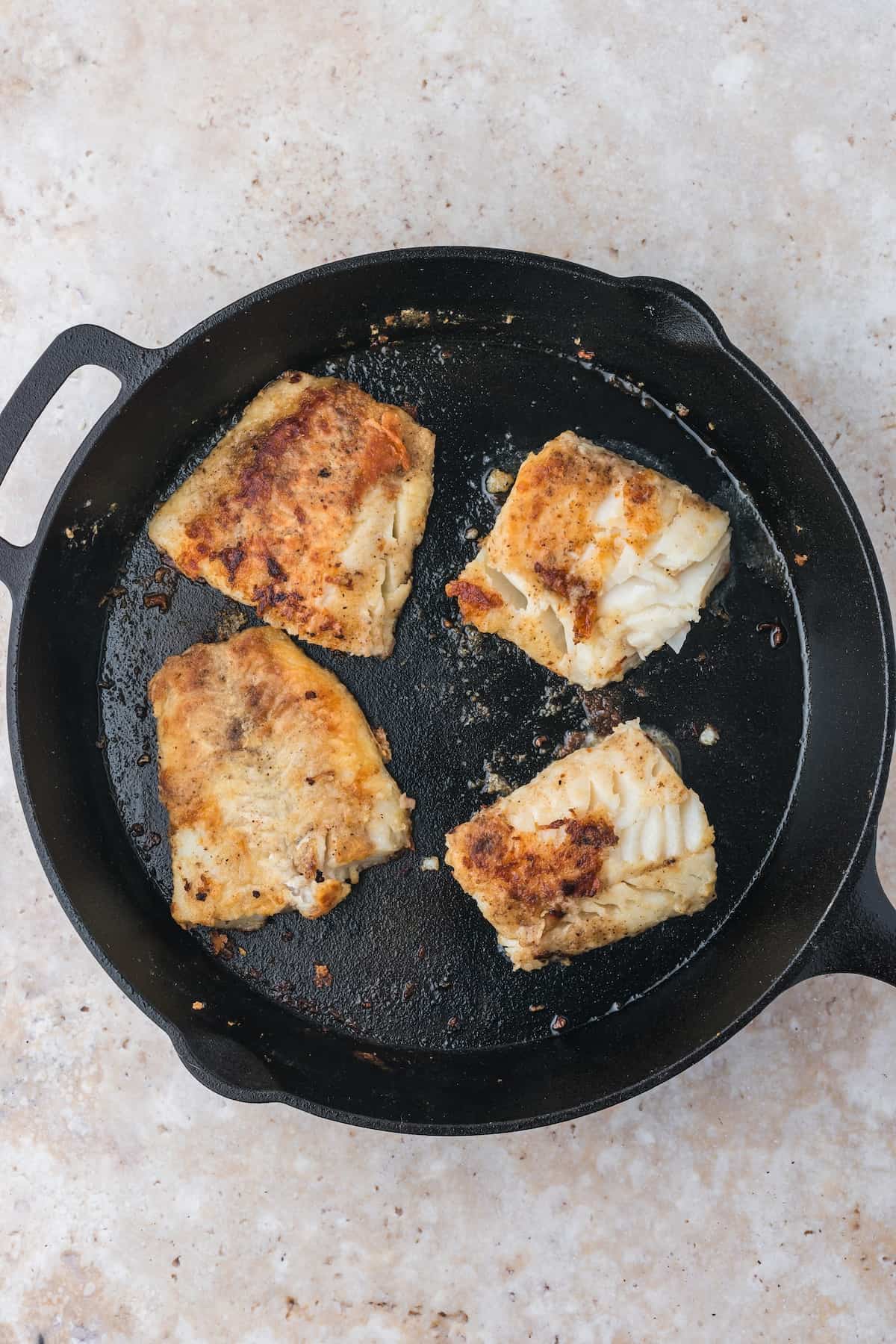 Pan-fried cod fillets in a cast iron skillet.