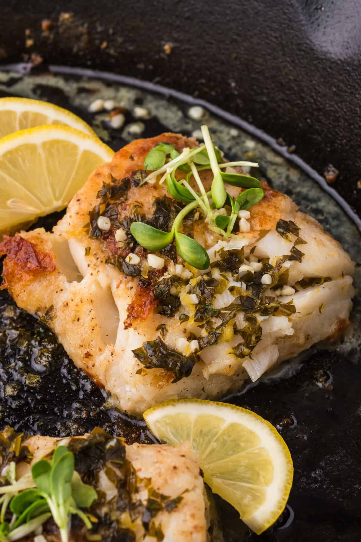 Seafood fillets in a skillet with lemon slices.