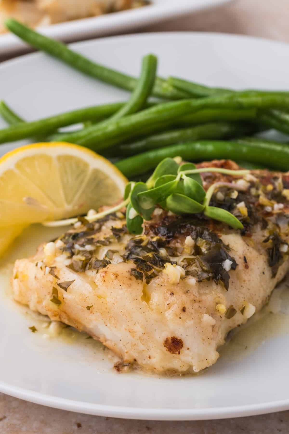 A plate with pan fried cod and green beans on it.