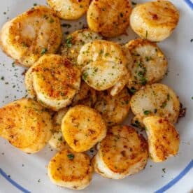 A plate of Perfect Pan Seared Scallops garnished with chopped herbs and seasonings, served on a white dish with a blue trim.