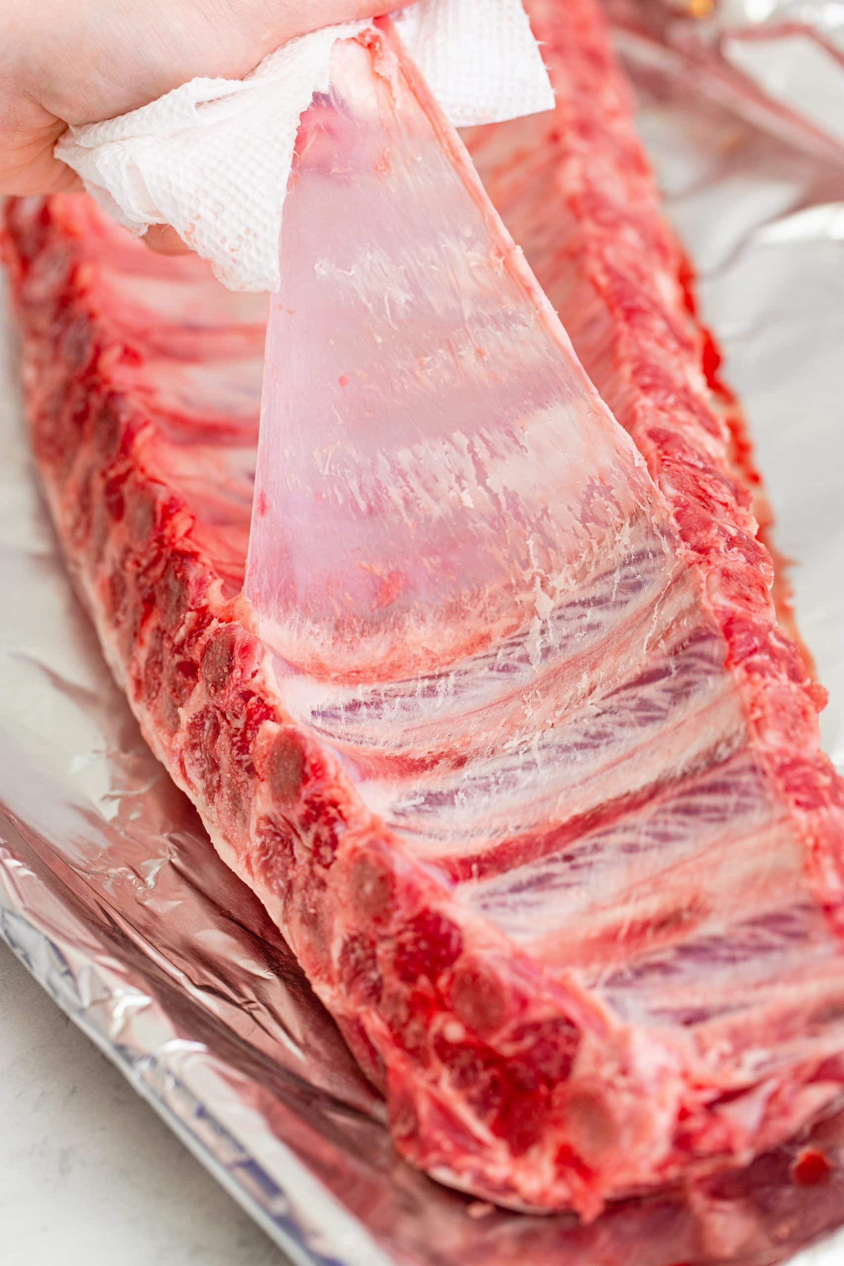 hand removing silver skin from rack of raw ribs