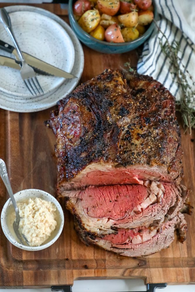 A baked ribeye roast with potatoes on a cutting board.