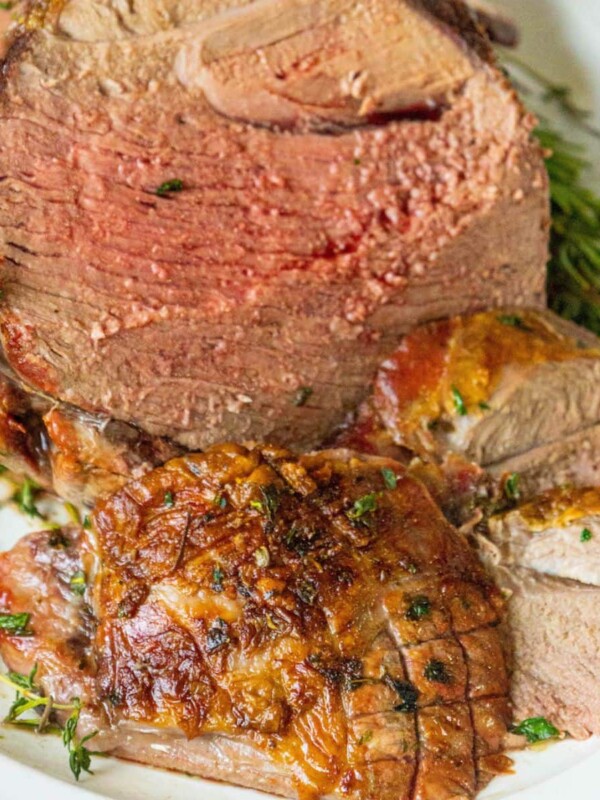 a roasted leg of lamb sliced open on a cutting board and topped with chopped herbs
