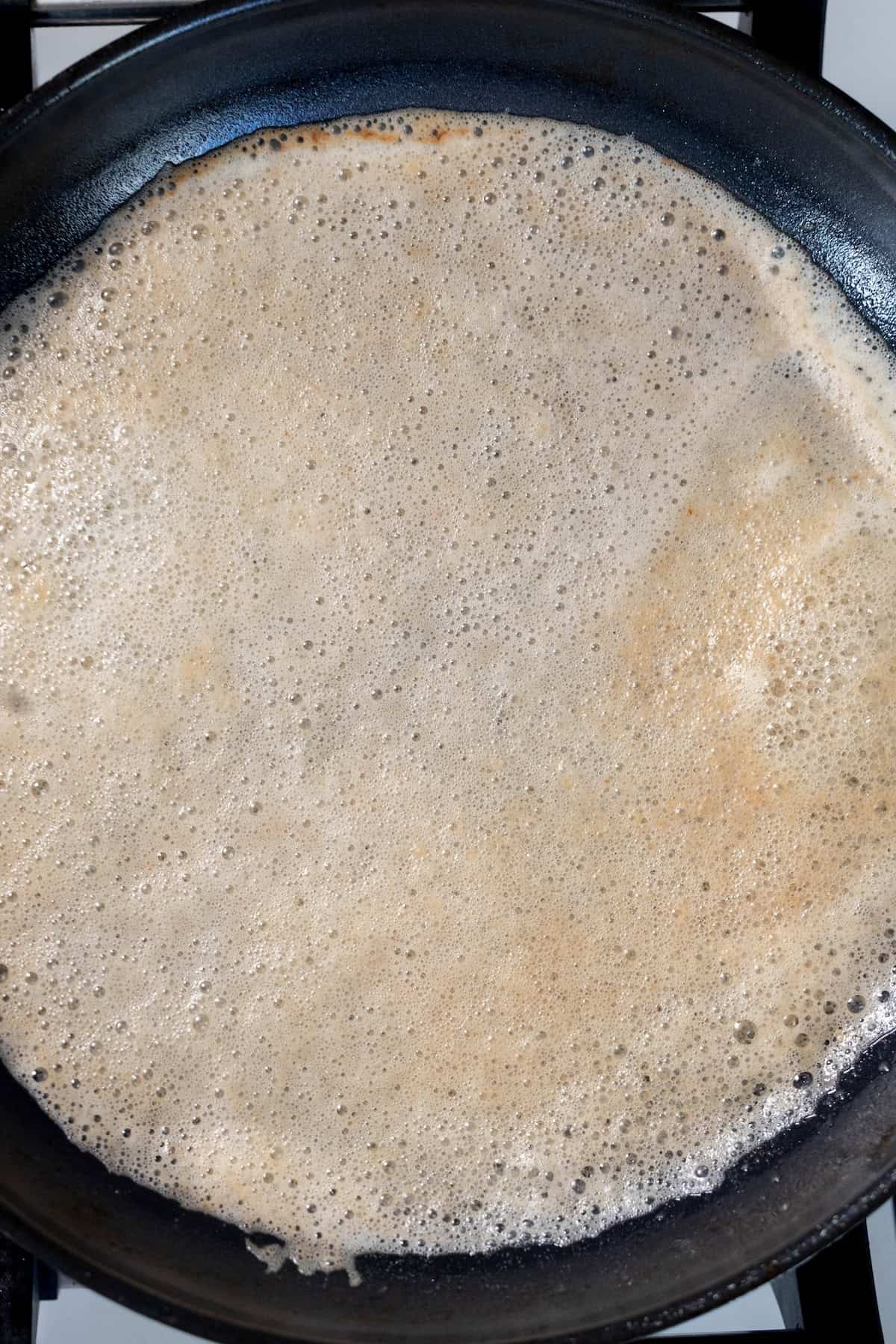 A thin crepe is cooking in a black frying pan on a stovetop, perfect for making sweet treatsโor even as a savory base for perfect pan seared scallops.
